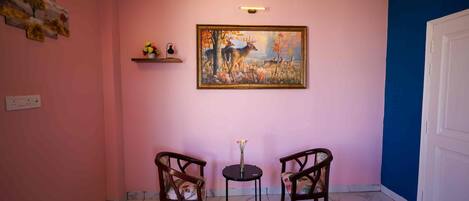 A hallway with pink walls, a painting of deer, two chairs, a small table with flowers, and a blue wall on the right.