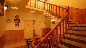 A wooden staircase with a handrail leading to an upper floor. A dining table with chairs is positioned in the foreground. - The Crosswoods Three (Kosiyakutoli)