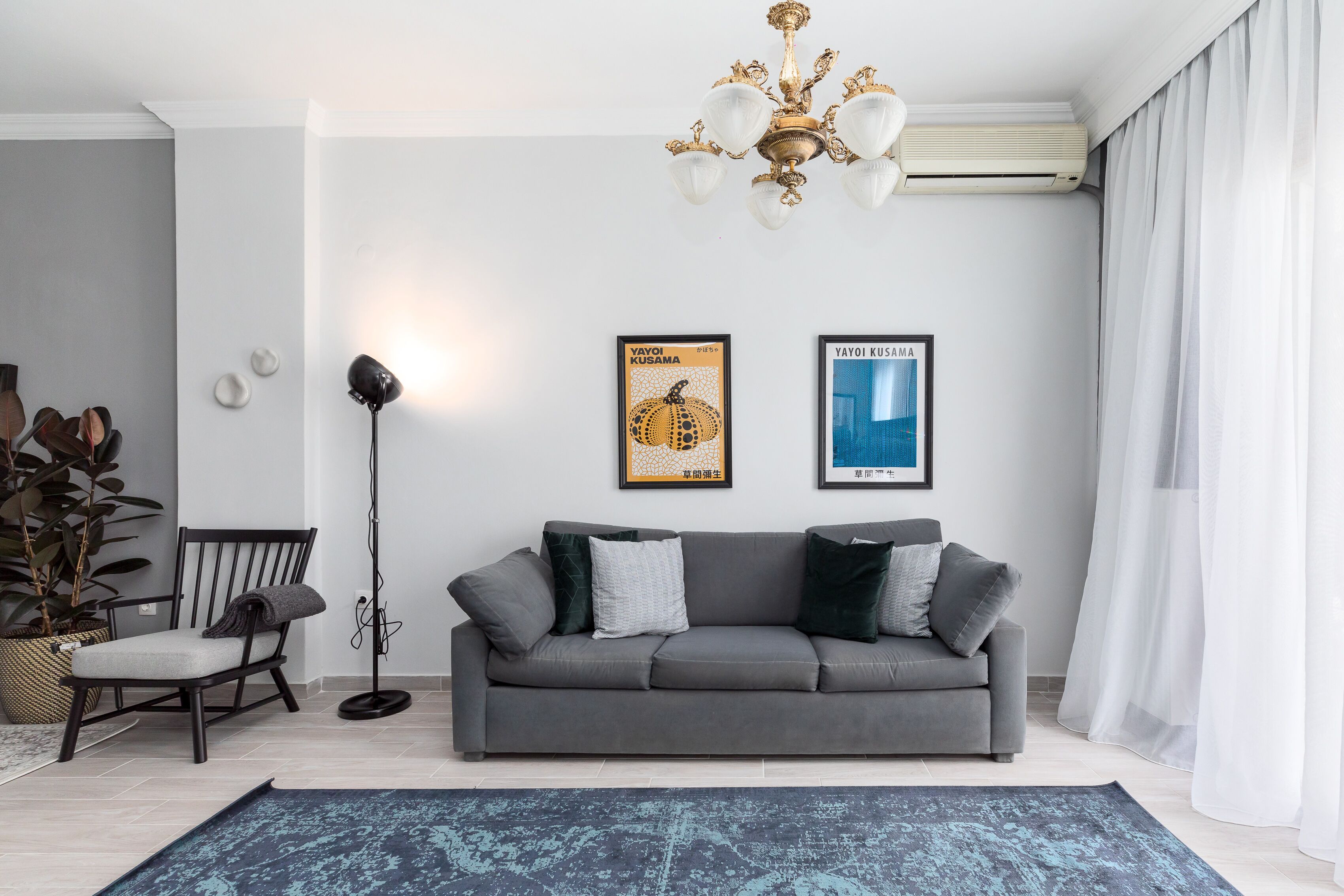 A modern living room with a grey sofa, a floor lamp, and two framed posters on the wall.