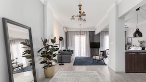 A modern living room with a large mirror, a chandelier, a grey sofa, and a dining area with chairs. - Pumpkin by halu' Lux 2BD-apartment (Thessaloniki)