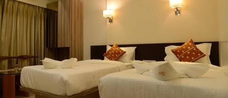 Habitación de hotel con dos camas, cada una con ropa de cama blanca y almohadas decorativas. Hay lámparas de pared a cada lado de las camas.
