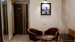 A room with a wooden door, a framed picture on the wall, a table with two chairs, and a bench. - THE MYRIAD HOTEL (Mumbai)