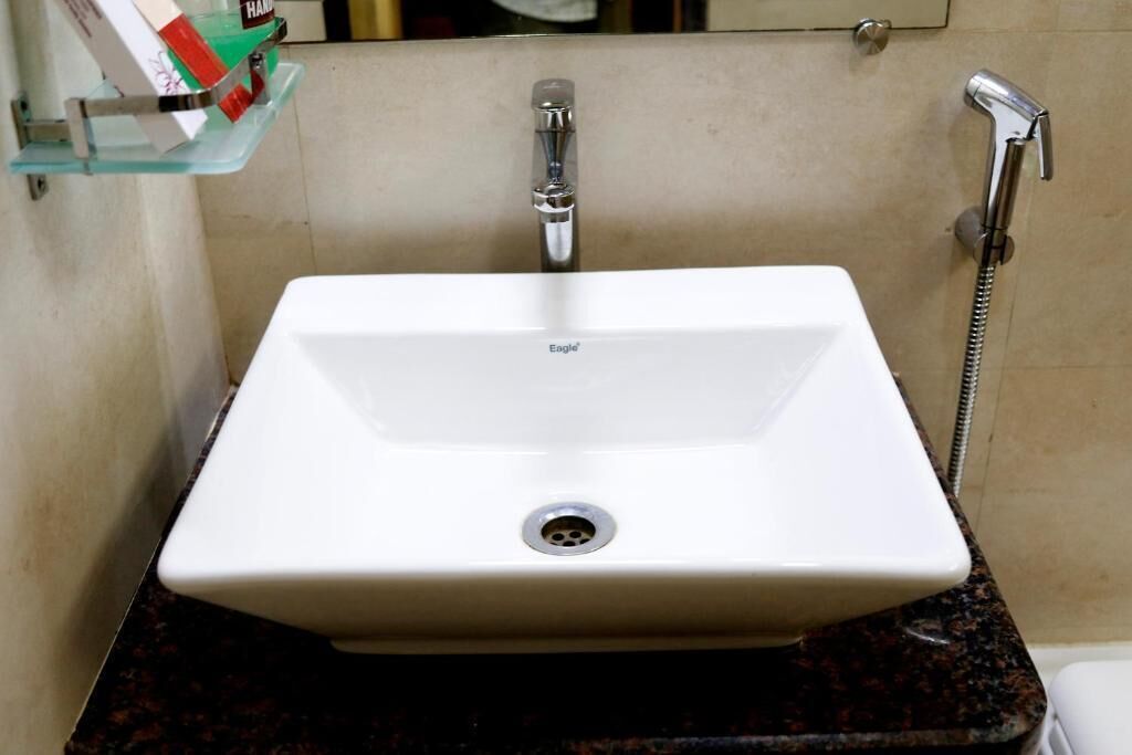 A bathroom with a white sink, a glass shelf with toiletries, and a shower.