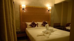A hotel room with a wooden headboard, a neatly made bed with white linens and decorative pillows, a bedside table, and a small desk with a chair. - THE MYRIAD HOTEL (Mumbai)
