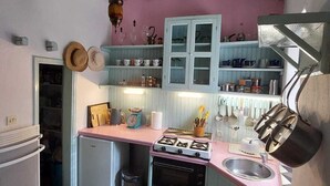 A compact kitchen with a gas stove, a sink, and a small refrigerator. There are shelves above the counter holding various kitchen items. - Beautiful, traditional Greek home with stunning views. (Glossa)