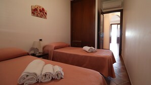 A hotel room with two beds, each with a neatly folded towel, a nightstand with a lamp, and a door leading to another room. - Vincenzo House (Castelluzzo)