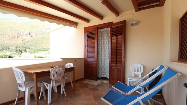 A balcony with a wooden table, two white chairs, and two blue lounge chairs. - Vincenzo House (Castelluzzo)