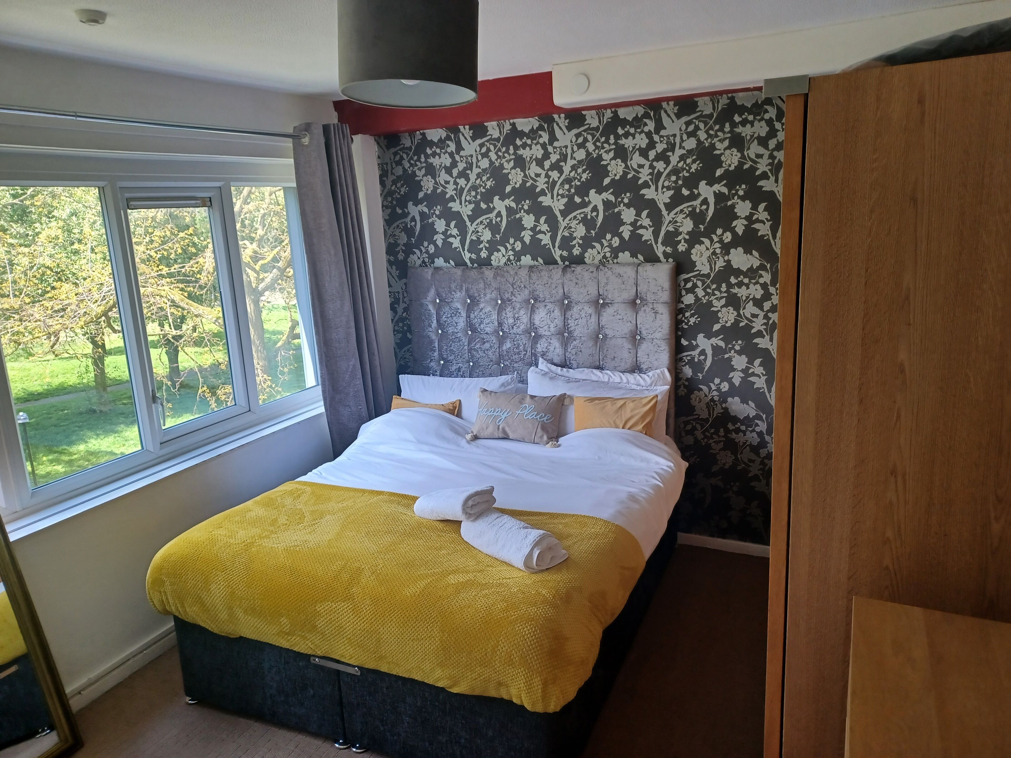 A bedroom with a large bed, a view of greenery outside, and a patterned wall.