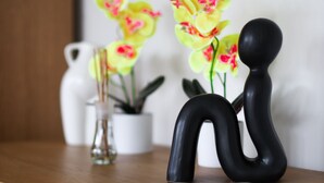 A black abstract sculpture on a wooden surface, a white vase with a plant, and yellow flowers in the background. - Lovely 1-bed Apartment in Birmingham (Birmingham)