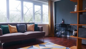 A modern living room with a sofa, a geometric rug, a wooden bookshelf, and a window with curtains. - Lovely 1-bed Apartment in Birmingham (Birmingham)