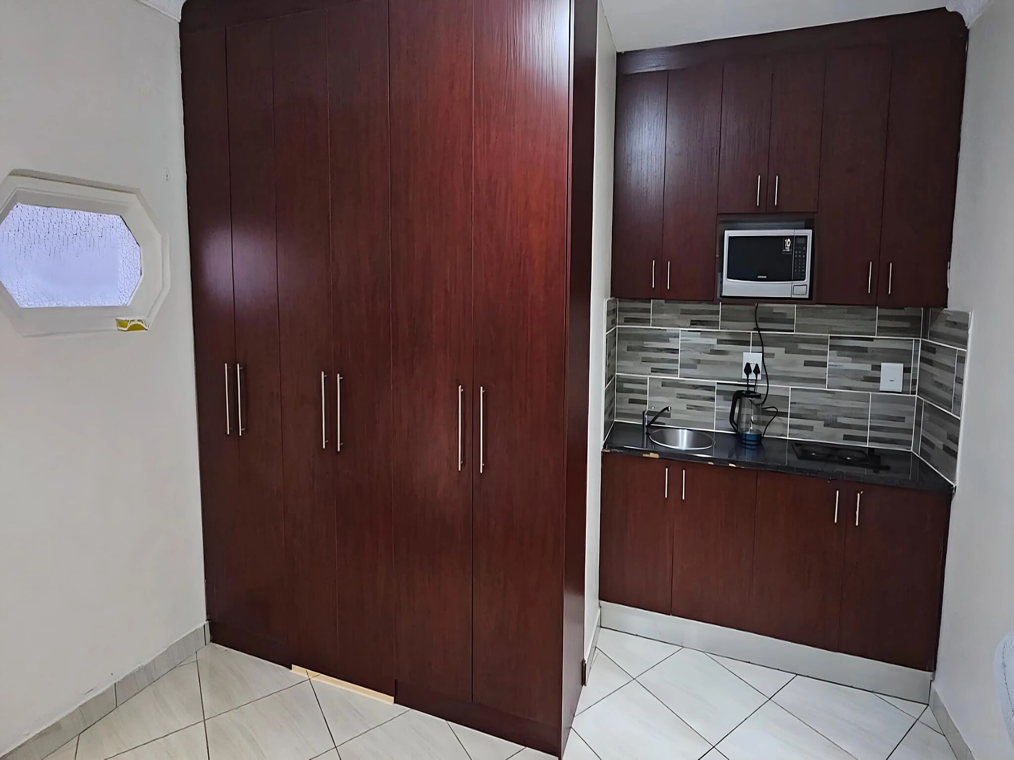 Una cocina con armarios de madera oscura, salpicadero de azulejos y microondas integrado.