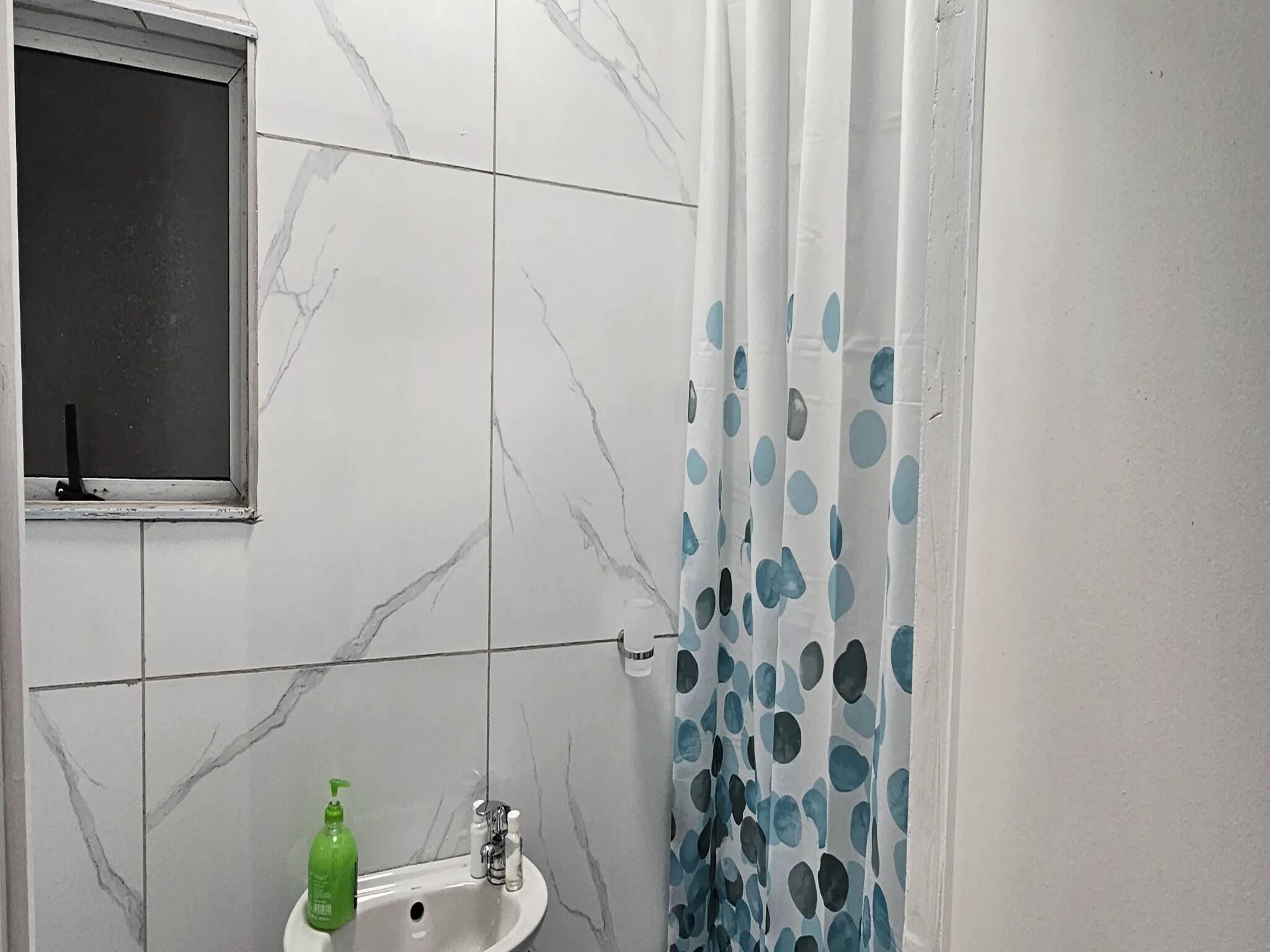 A bathroom with a white sink, a window, and a shower curtain with blue polka dots.