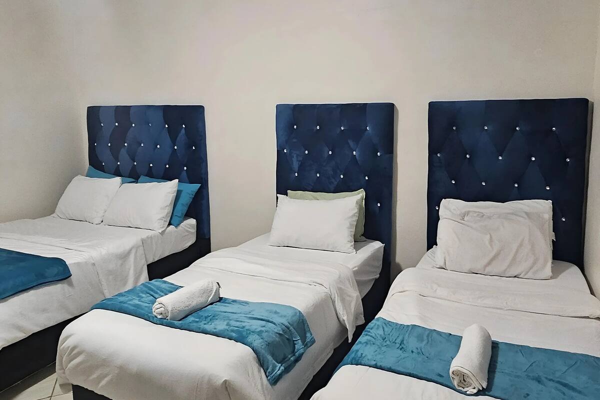 Tres camas individuales con cabeceros azules y ropa de cama blanca, dispuestas en fila en una habitación de hotel.