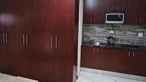 A kitchen with dark wooden cabinets, a stainless steel sink, and a microwave. - Goshen Lodge Spencer (Cape Town)