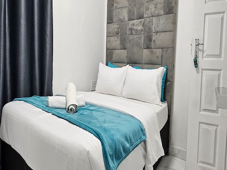 A neatly made bed with white bedding and a teal throw blanket, a white pillow, and a rolled towel on the bed.