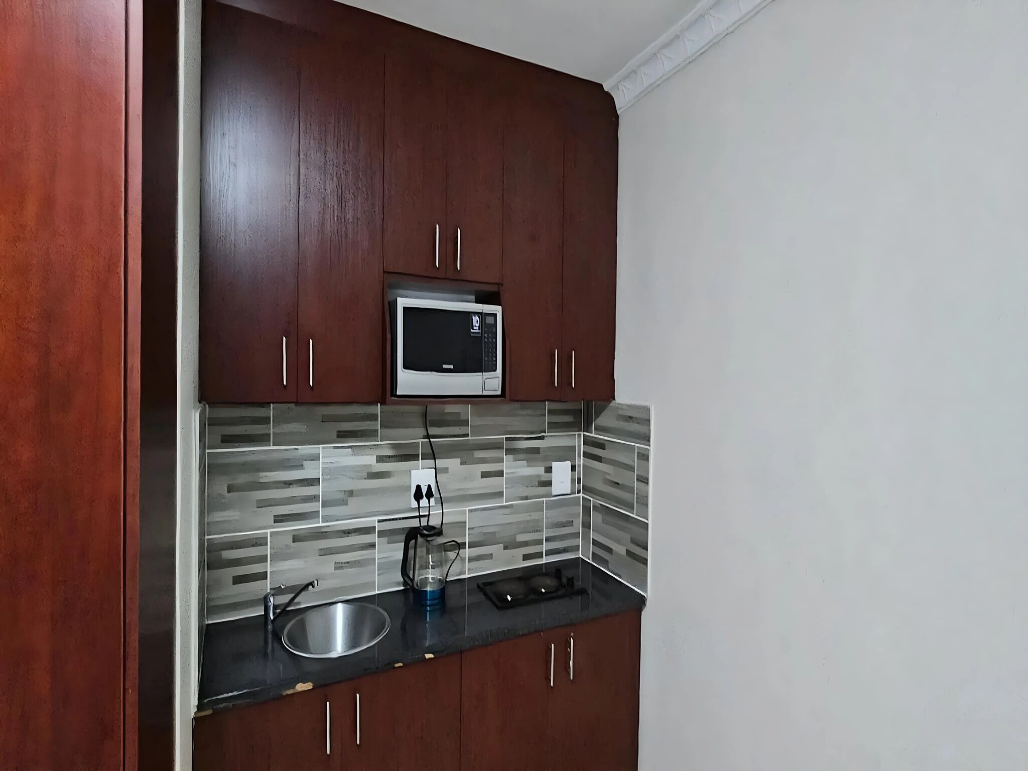 A kitchen with dark wooden cabinets, a stainless steel sink, a microwave, and a tiled backsplash.
