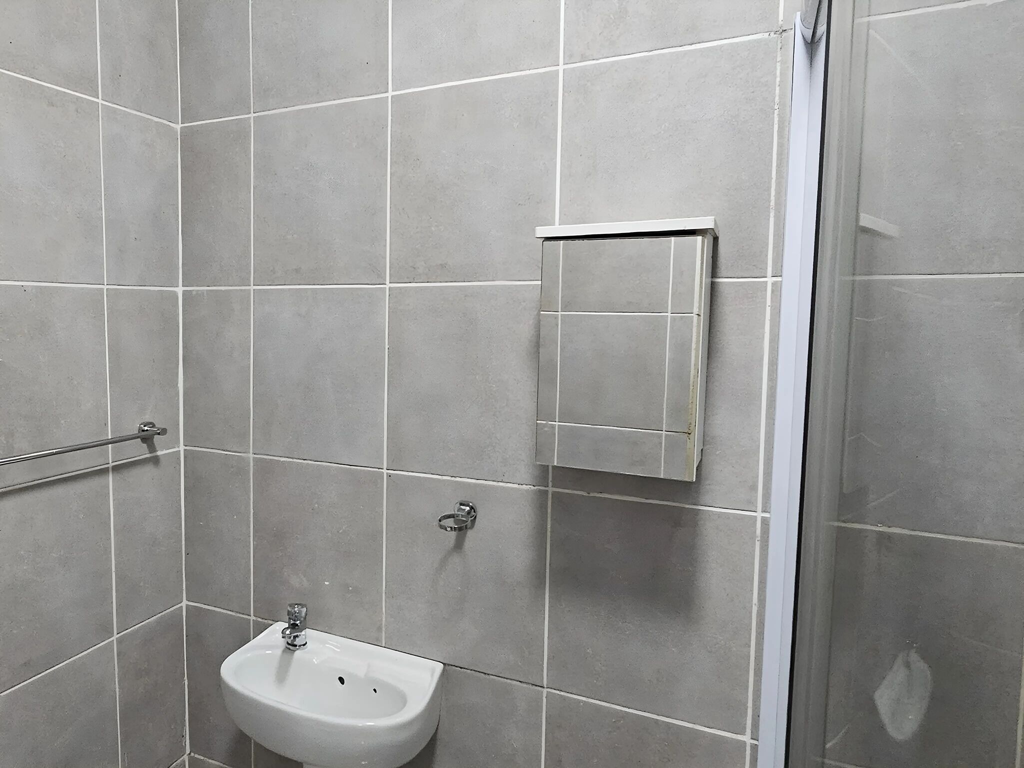 Un baño con baldosas grises, un lavamanos blanco y un espejo.