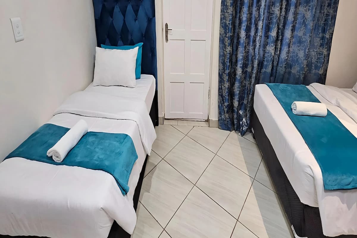 Habitación de hotel con dos camas individuales, cada una con cabecera azul y ropa de cama blanca.