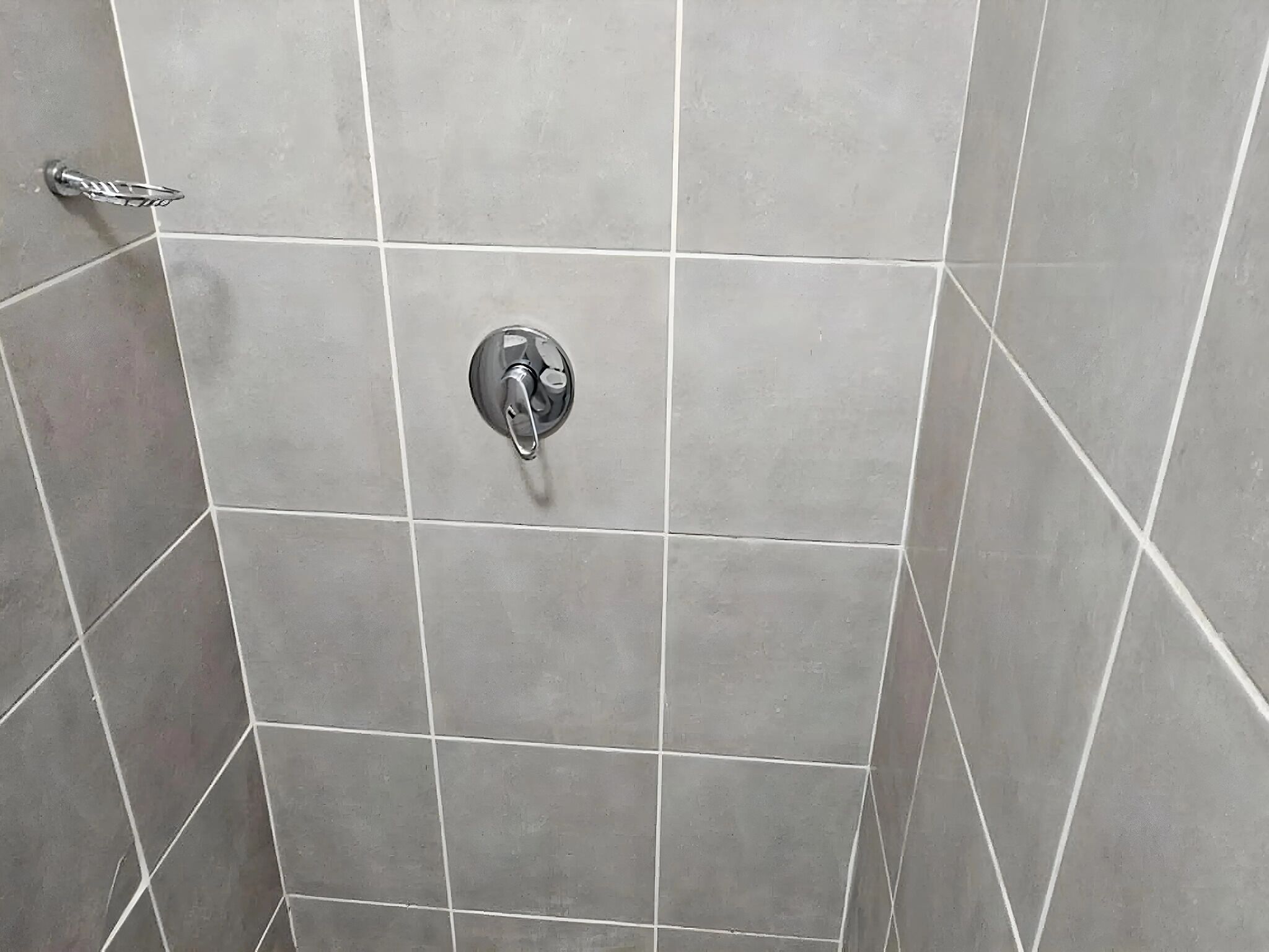 A bathroom with grey tiles, a shower control knob, and a handrail.
