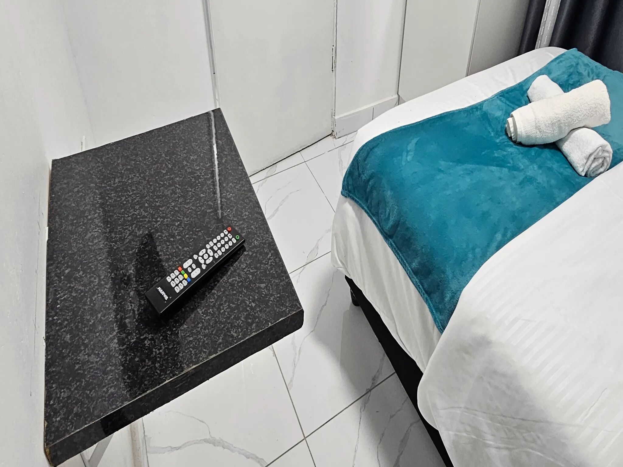 Une chambre d’hôtel avec un lit, une table de chevet noire et une télécommande.