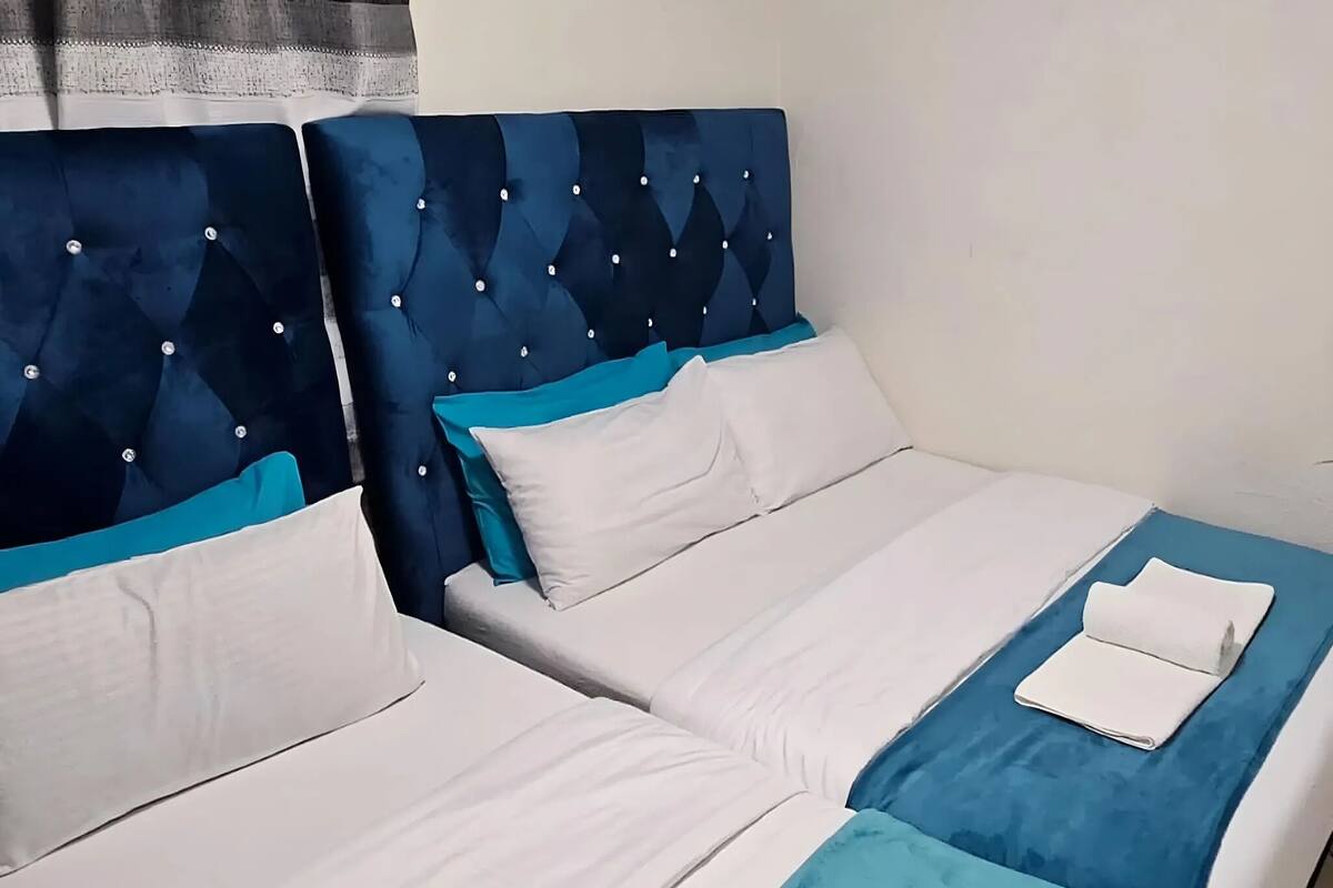 Habitación de hotel con dos camas, cada una con cabecero azul y ropa de cama blanca.