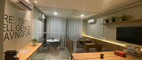 A modern office space with a glass partition, a wooden reception desk, a conference table, and a mounted TV.