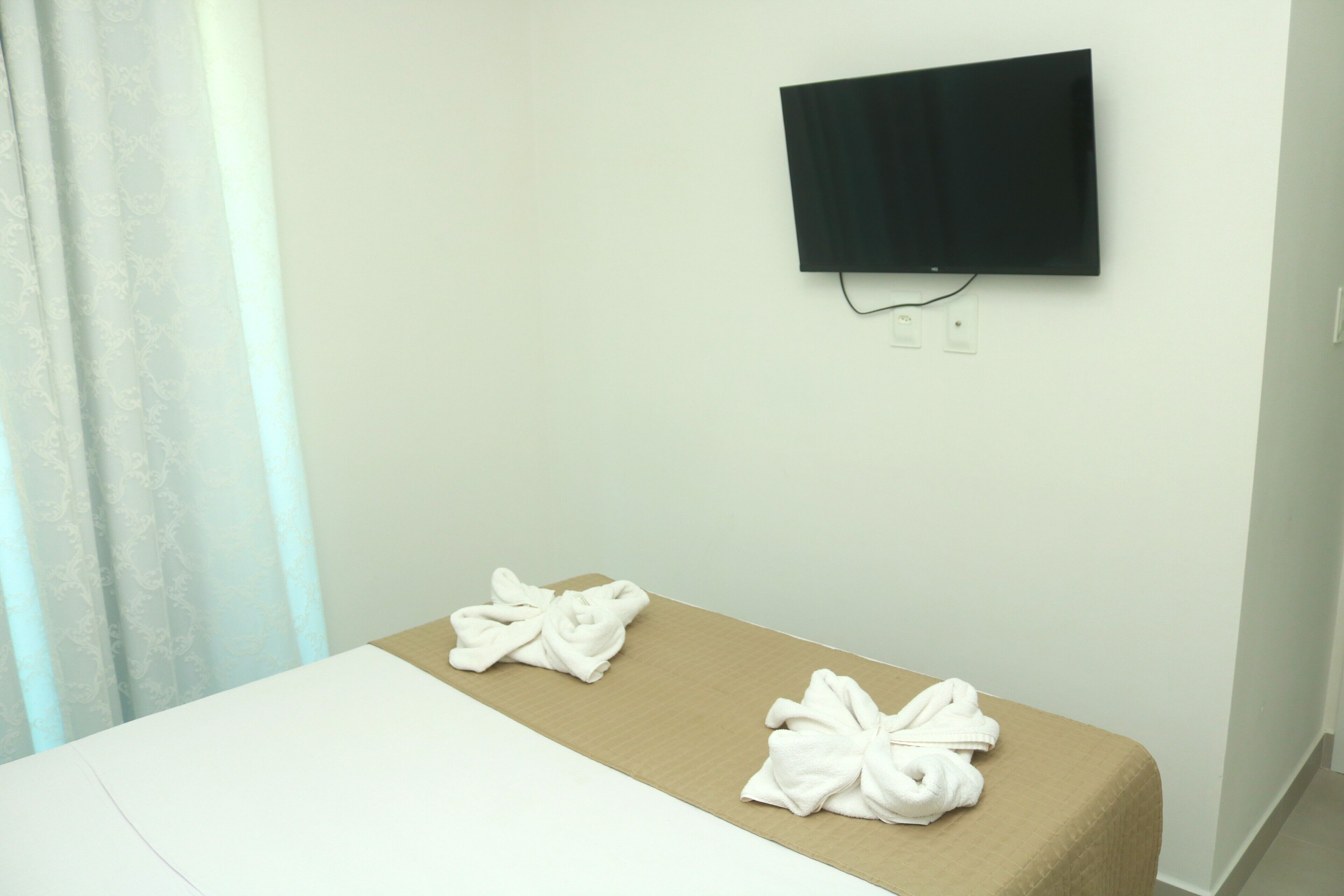 Ein Hotelzimmer mit einem Bett, einem an der Wand montierten Flachbildfernseher und zwei Handtüchern auf dem Bett.