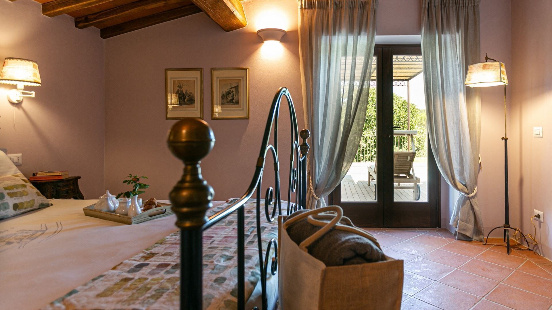 Un dormitorio con cama, una mesita de noche con libros, una lámpara y una ventana con cortinas.
