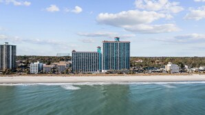 Un hotel frente al mar con varios edificios altos, una playa en primer plano y un cielo despejado.