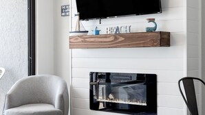 Una sala de estar moderna con un televisor de pantalla plana sobre una chimenea, un sillón gris y una mesa de centro.