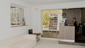 A modern living room with a white sofa, a TV, and a bookshelf filled with books and magazines. - HOSTAL TAHITI RS (Salou)