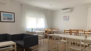 A room with a sofa, a dining table with chairs, and a window with blinds. - HOSTAL TAHITI RS (Salou)