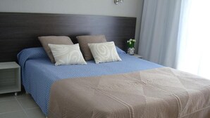 A neatly made bed with a blue and beige bedspread, a dark headboard, and a small bedside table with a vase of flowers. - HOSTAL TAHITI RS (Salou)