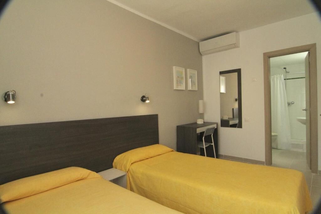 A hotel room with two beds, a desk, a mirror, and a shower area.
