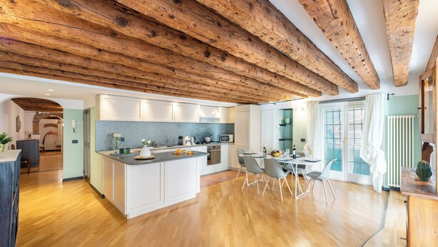 Una cocina moderna con vigas de madera, una isla central y un comedor con sillas.