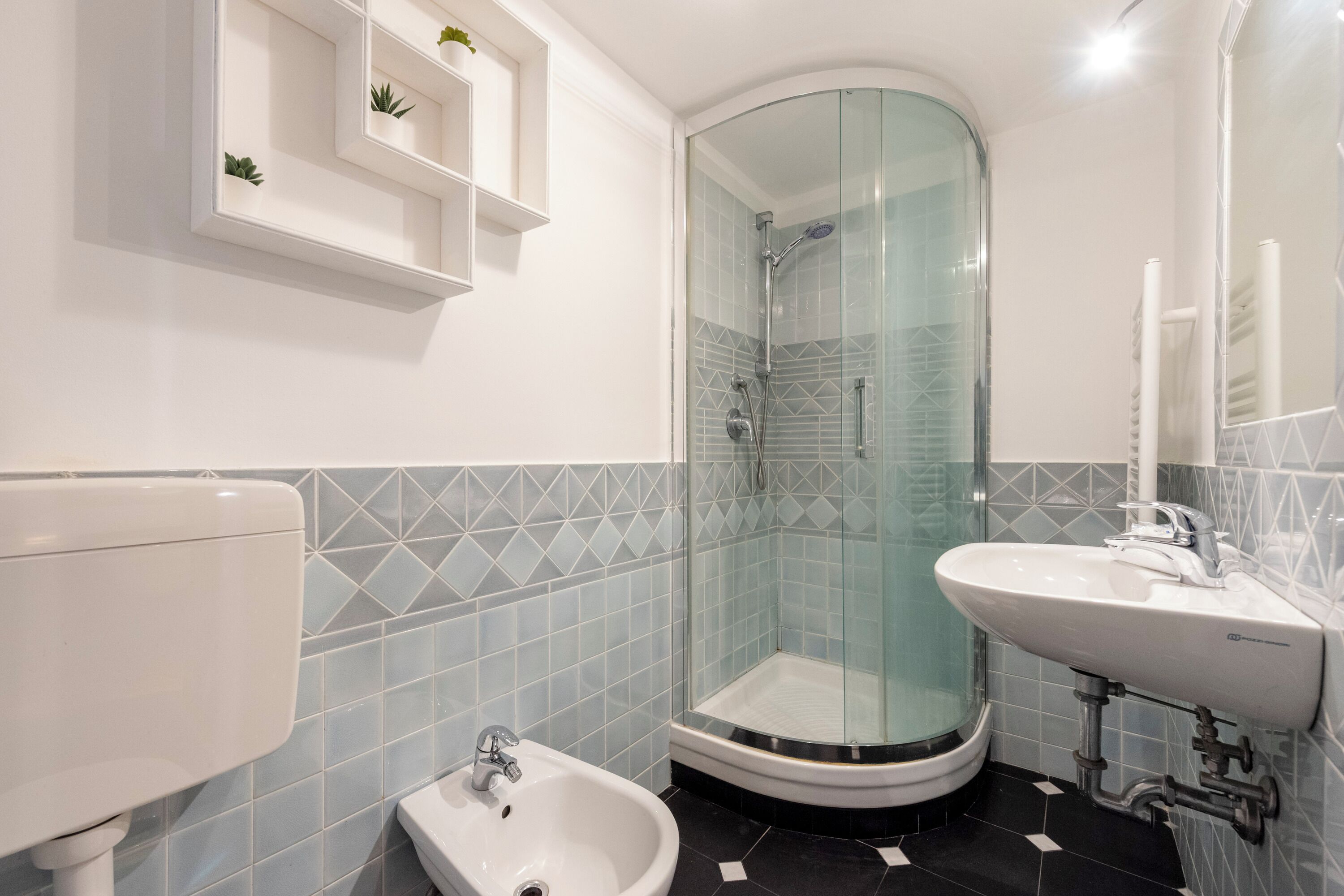 A modern bathroom with a glass-enclosed shower, a white sink, and a bidet.