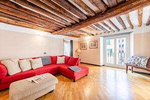 A living room with a red sectional sofa, wooden flooring, a wooden ceiling, and a view through a glass door.