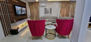 A modern living room with a TV, two red chairs, a sofa, and a decorative table. - Luxury 3-bed House in Gated Estate With Pool Lekki (Lekki)