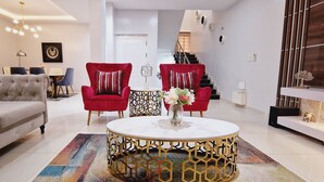 A modern living room with a grey sofa, red armchairs, a round coffee table with a gold base, and a colorful rug. - Luxury 3-bed House in Gated Estate With Pool Lekki (Lekki)