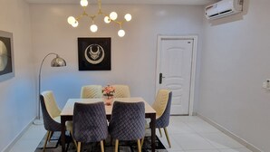A dining area with a table and chairs, a pendant light, wall art, and an air conditioning unit. - Luxury 3-bed House in Gated Estate With Pool Lekki (Lekki)