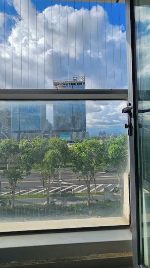 A view through a window with a metal grid, a road with trees, and a distant building. - RHO HOTEL (Shenzhen)