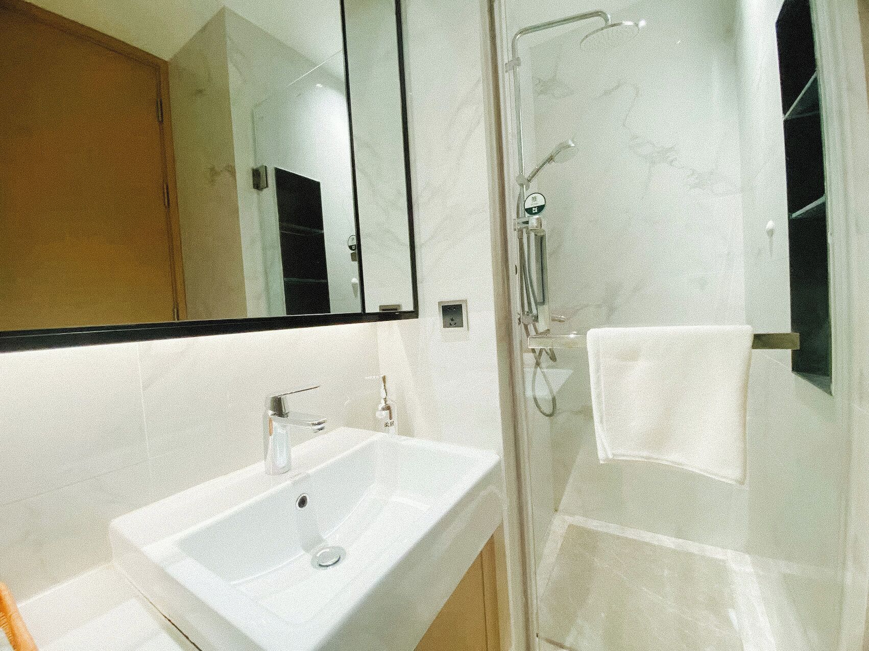 Un baño con un lavabo blanco, un espejo, ducha con puerta de vidrio y una toalla colgada en la pared.
