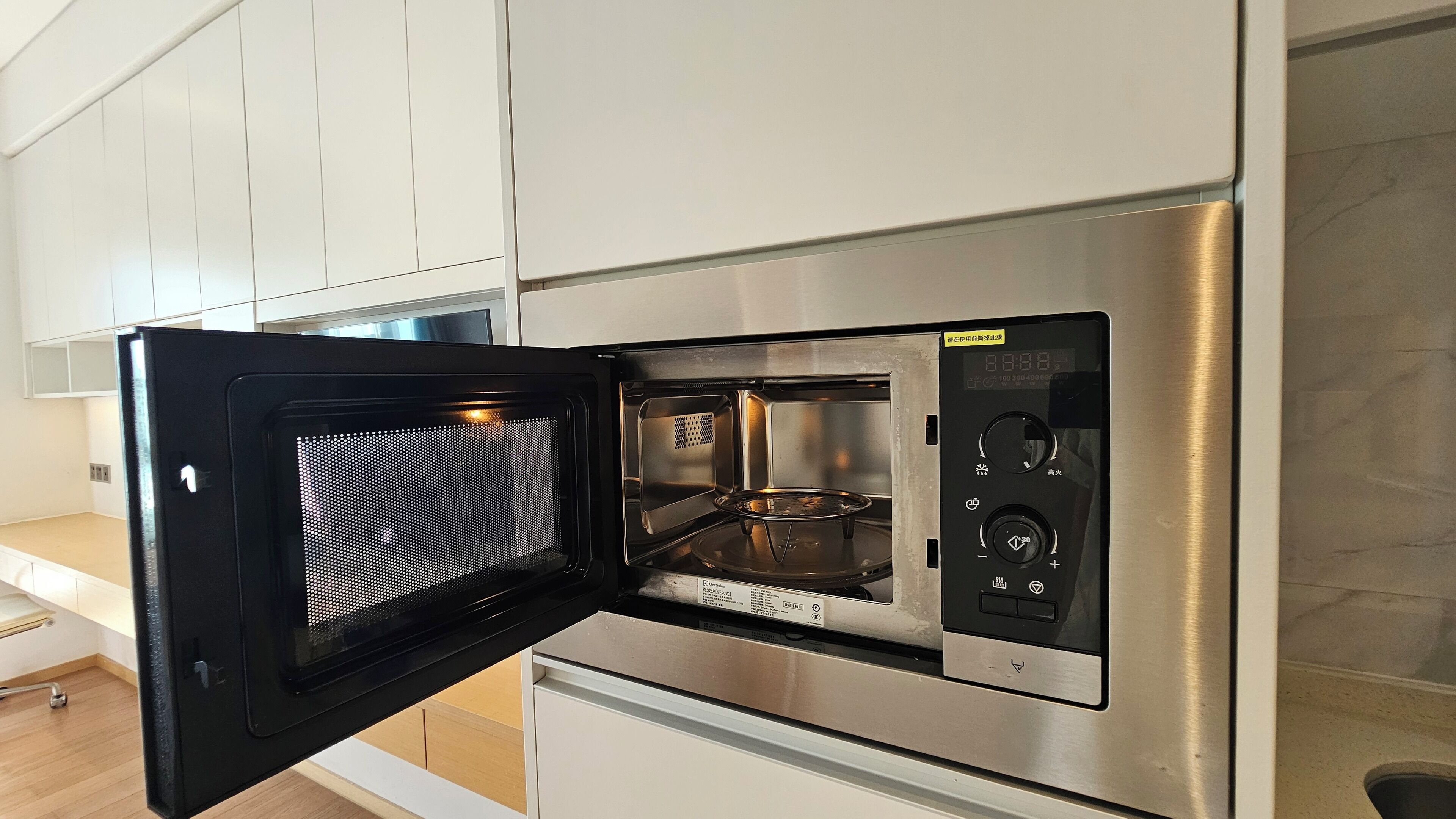 Una cocina con microondas y horno integrados, electrodomésticos de acero inoxidable y muebles de cocina blancos.