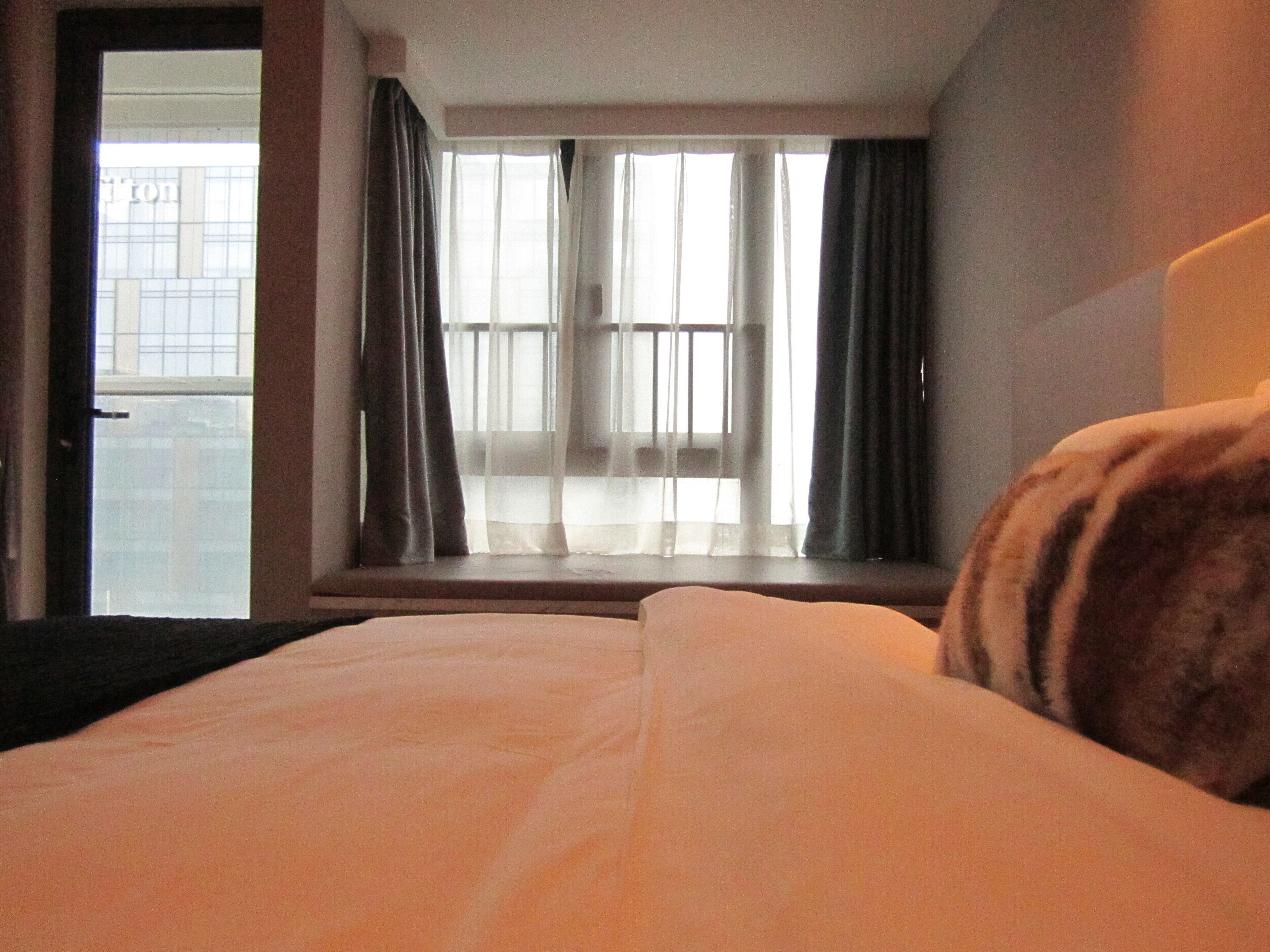 A hotel room with a bed, a window with curtains, and a view of a building outside.