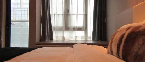 A hotel room with a bed, a window with curtains, and a view of a building outside.