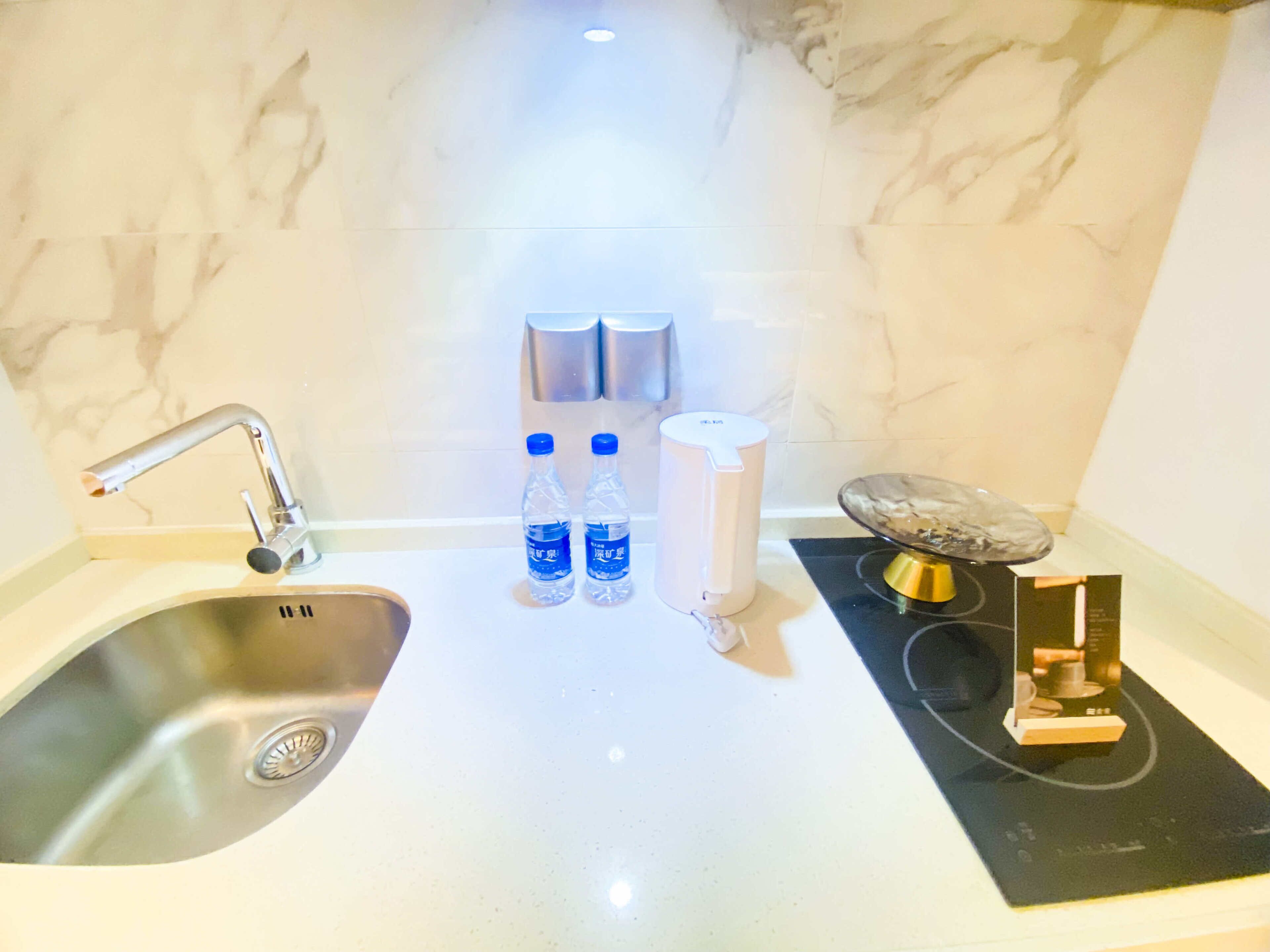 A bathroom with a sink, two bottles of water, a soap dispenser, and a small round mirror.