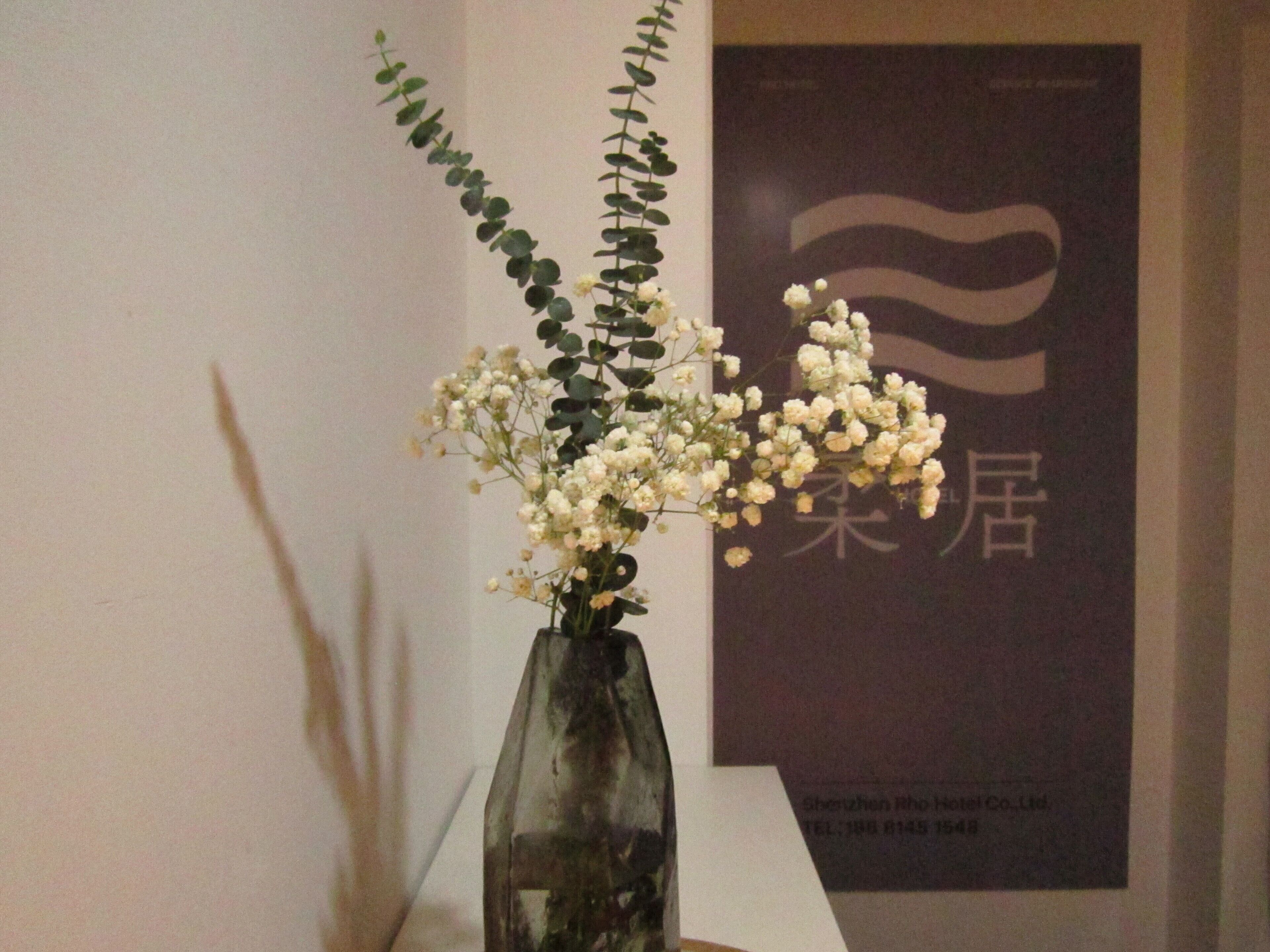 Eine Glasvase mit weißen Blumen und grünem Grün auf einem Tisch.