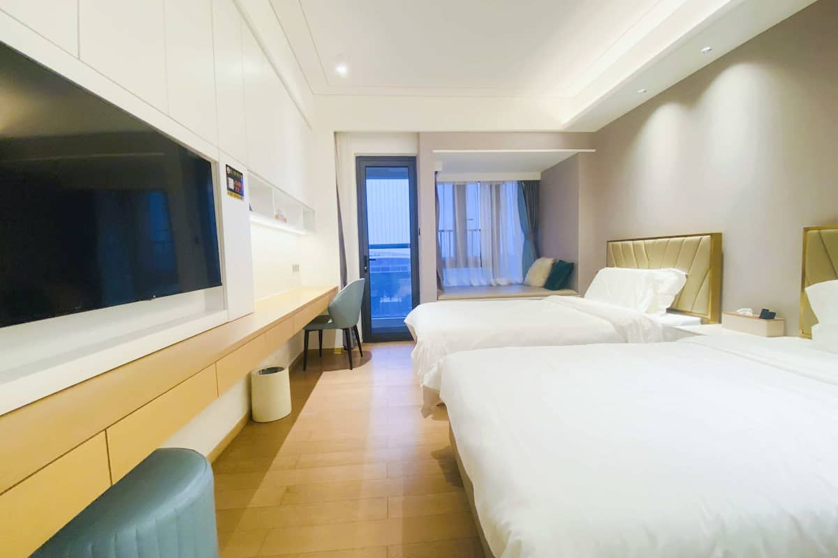 Ein Hotelzimmer mit zwei Betten, einem Fernseher, einem Schreibtisch und Blick auf den Balkon.