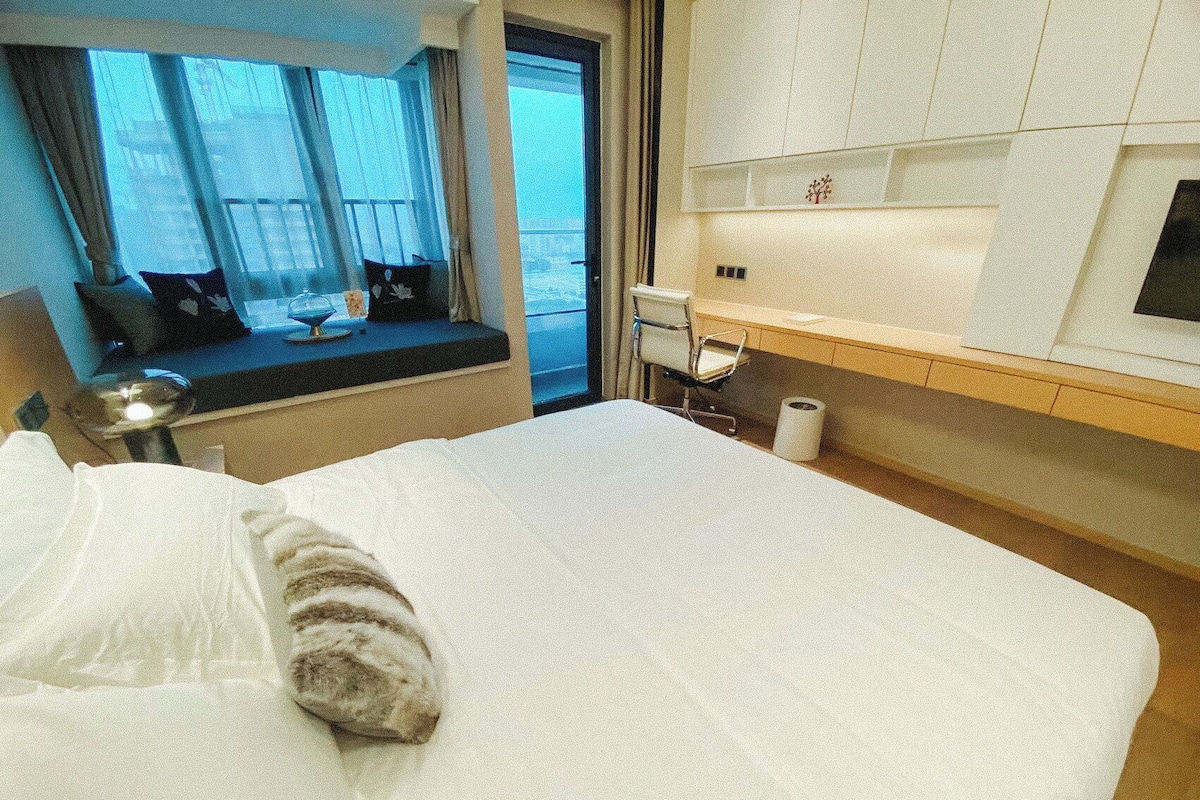Ein Hotelzimmer mit Bett, Schreibtisch, Stuhl, einem Fenster mit Vorhängen und Blick nach draußen.