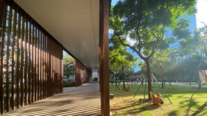 Un paseo techado de diseño moderno que conduce a un parque con columpios y árboles.